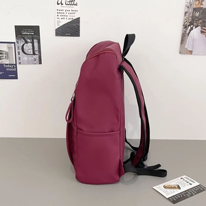 Side view of dark red backpack with matte texture and side pocket in lifestyle setting