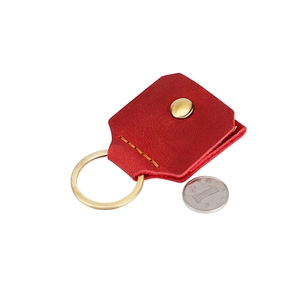 Détail d'un étui porte-clés en cuir rouge avec bouton-pression doré et couture jaune