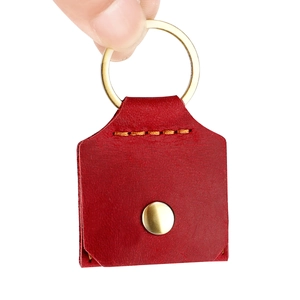 Détail du porte-clés en cuir rouge foncé avec bouton doré et coutures à la main