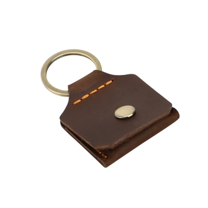 Détail macro du porte-clés en cuir marron foncé avec coutures orange et bouton pression