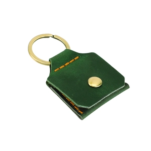Détail du porte-clés en cuir vert foncé avec coutures oranges et bouton pression doré