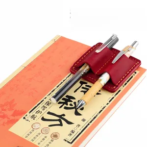 Detail of vintage red leather pen holder clip with dual slots on a notebook cover