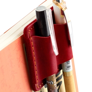 Close-up of wine red leather double pen holder with orange stitching on a notebook