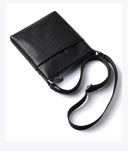 Detailed view of black pebbled leather crossbody bag with adjustable fabric strap and metal zip