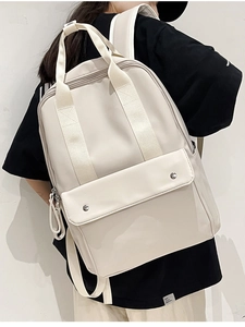 Detail view of beige backpack with metal snaps and top handles on a model