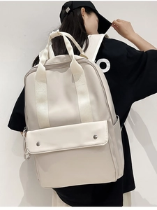 Detailed view of a beige minimalist backpack featuring front flap pockets and large capacity