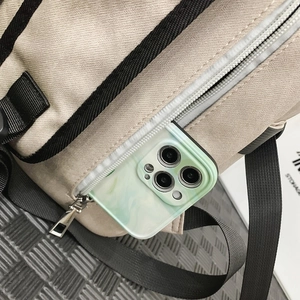Detail of the side zipper pocket on a beige backpack showing large storage for a smartphone
