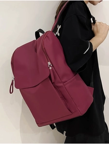 Side view of a wine red nylon backpack worn by a model against a white wall