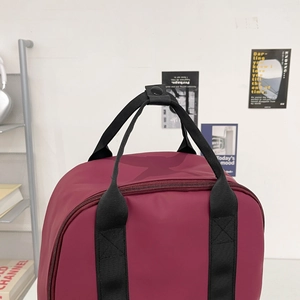 Top detail of wine red waterproof nylon backpack with dual handles and metal snap closure