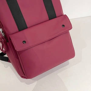 Close-up of burgundy leather backpack with black metal snap buttons and woven strap details
