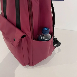 Detail of burgundy backpack side pocket holding a water bottle and front flap pocket