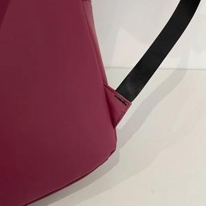 Macro shot of reinforced triangular stitching on burgundy faux leather backpack strap