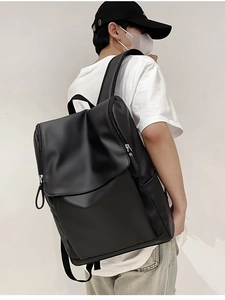 Side view of a sleek black minimalist travel backpack worn by a model against a wall