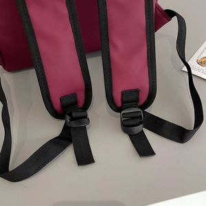 Detail of padded burgundy backpack shoulder straps with adjustable black plastic buckles