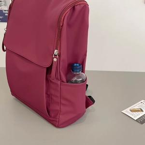 Side view of burgundy nylon travel backpack featuring side pockets and water-resistant fabric