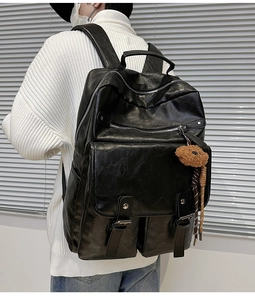 Detail of a black leather backpack with metal buckles and a cute teddy bear charm