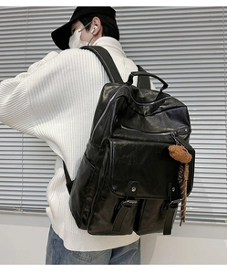 Side view of black textured leather backpack featuring double metal buckles and a bear charm