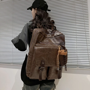 Brown leather backpack with brown bear charm shown on model in a minimalist setting