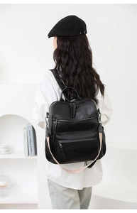 Detalle de la mochila de cuero negro con cremalleras y correa tejida decorativa