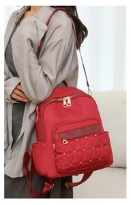 Detail view of red oxford fabric backpack featuring gold hardware and diamond quilted pockets