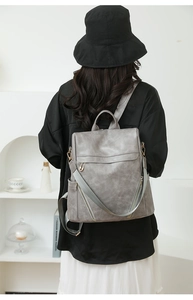Rear view of a vintage gray PU leather backpack with a removable woven shoulder strap