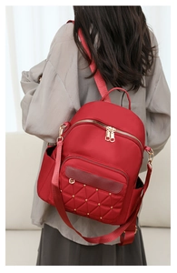 Detail of red quilted oxford backpack with gold rivets and dual zipper on model back