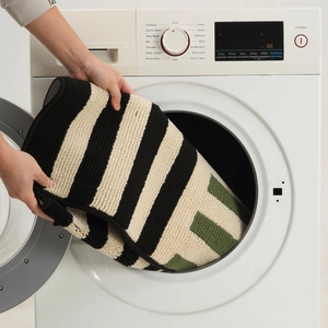 Nordic striped bath mat in green, white and black being placed into a washing machine