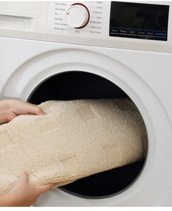Close-up of putting a soft beige machine-washable rug with geometric pattern into a laundry machine