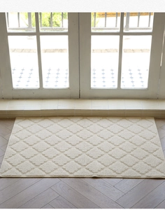 Detail of cream doormat with textured diamond pattern on herringbone wood floor