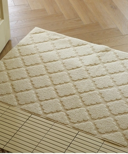 Close-up of cream entryway mat with 3D embossed clover pattern on wood floor