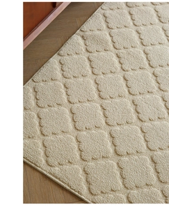 Detail of cream doormat with embossed fan-square texture on herringbone wood floor