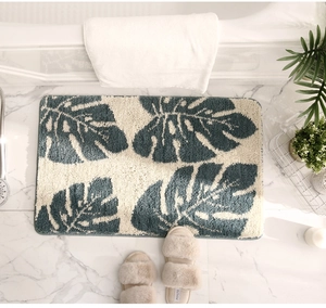 Detail of thick absorbent bathroom mat with green monstera leaf pattern on marble floor