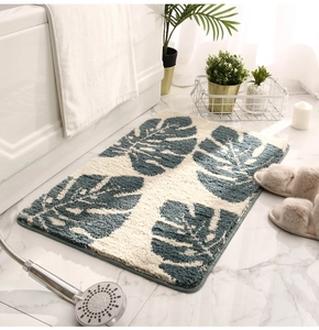 Thick non-slip bath mat with green monstera leaf pattern on marble floor detail