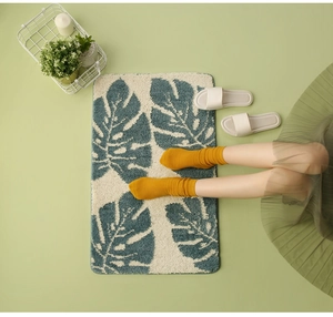Detail of rectangular bath mat featuring green monstera leaf pattern on cream background
