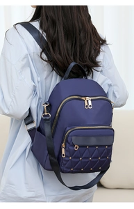 Detail of dark blue Oxford backpack showing quilted diamond pattern and gold rivets on a model