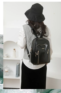 Rear view of model wearing a black PU leather backpack with multi-zipper pockets