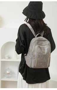 Detailed view of grey faux leather backpack with multiple gold zippers and large capacity
