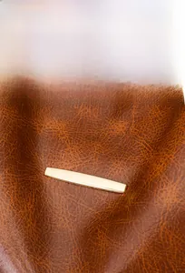 Detail of soft brown pebble leather with a polished gold metal strip on a backpack