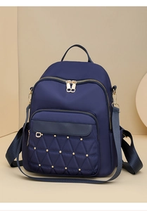 Close-up of quilted navy blue oxford backpack featuring gold metal studs and zippers