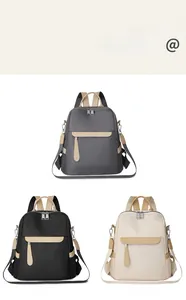 Three minimalist nylon backpacks in gray, black, and cream with leather pull tabs