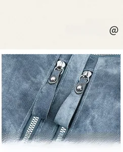 Detail of dual metal zippers on washed denim bag with riveted pullers and twill texture