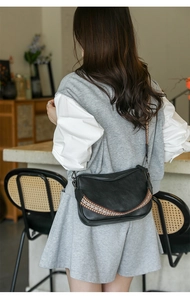 Detail of black leather crossbody bag with bohemian patterned strap and metal hardware