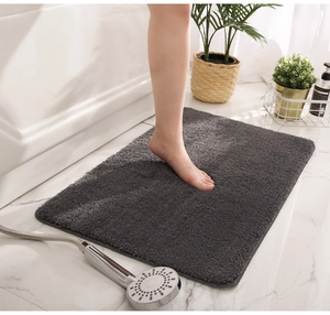 Detail of dark gray plush non-slip bathroom mat on white marble floor with plants