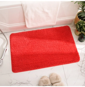 Close-up of fluffy red absorbent bathroom rug on white marble floor with cozy bath scene