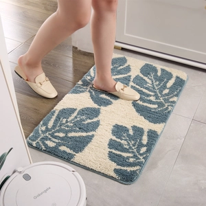 Absorbent rectangular bath mat with blue monstera leaf pattern on cream plush surface