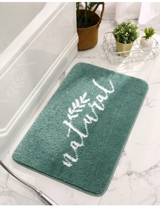 Dettaglio del tappeto da bagno verde con texture floccata e scritta Natural
