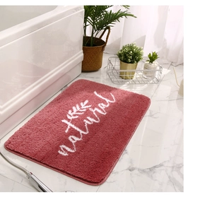 Dettaglio del tappetino da bagno rosa morbido con scritta natural su marmo