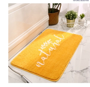 Dettaglio del tappetino da bagno giallo con ricamo di foglie su pavimento in marmo