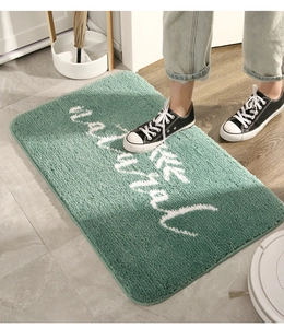 Dettaglio del tappeto da bagno verde bosco a pelo lungo con scritta natural e fibre