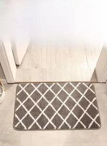 Detail of plush grey and white argyle bath mat showing high-quality edge stitching and soft texture